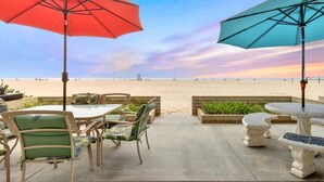 A patio with outdoor seating, two umbrellas, and a view of the beach. - West Newport Oceanfront Home & Patio on 65th St. (Newport Beach)