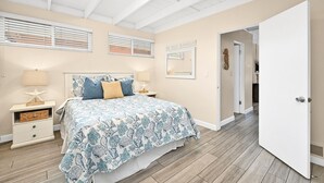 Un dormitorio con cama, mesitas de noche, una lámpara con forma de estrella de mar, un espejo y una puerta que da a otra habitación.