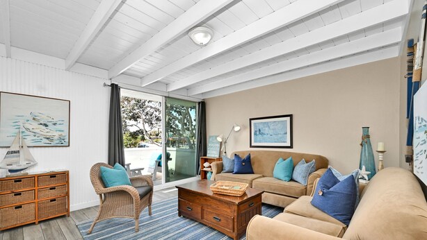 Una sala de estar con un ventanal grande, muebles de mimbre, un sofá color beige y un tapete azul a rayas.
