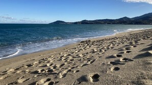 Una playa con huellas en la arena, cielo despejado y montañas a lo lejos.