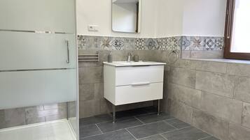 Een moderne badkamer met een douchecabine van glas, een witte wastafel met een spiegel erboven en behangtegels op de muren.