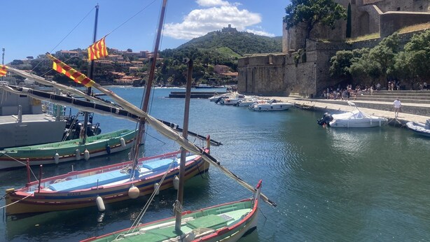 Un puerto con barcos amarrados, una estructura que parece un castillo y una colina con edificios al fondo.