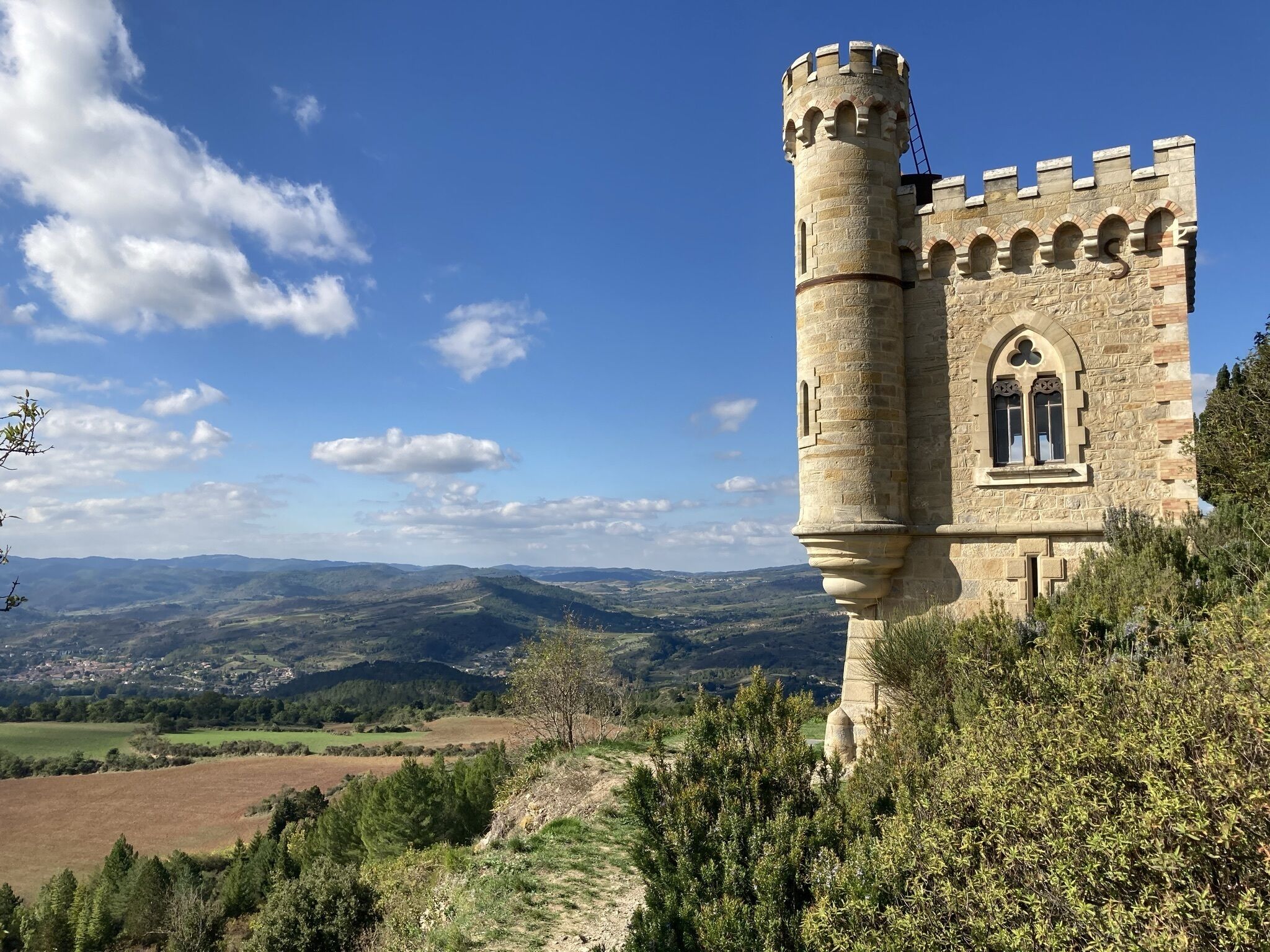 Una torre de piedra histórica con almenas, un amplio ventanal de arco y vistas a colinas ondulantes y un valle.