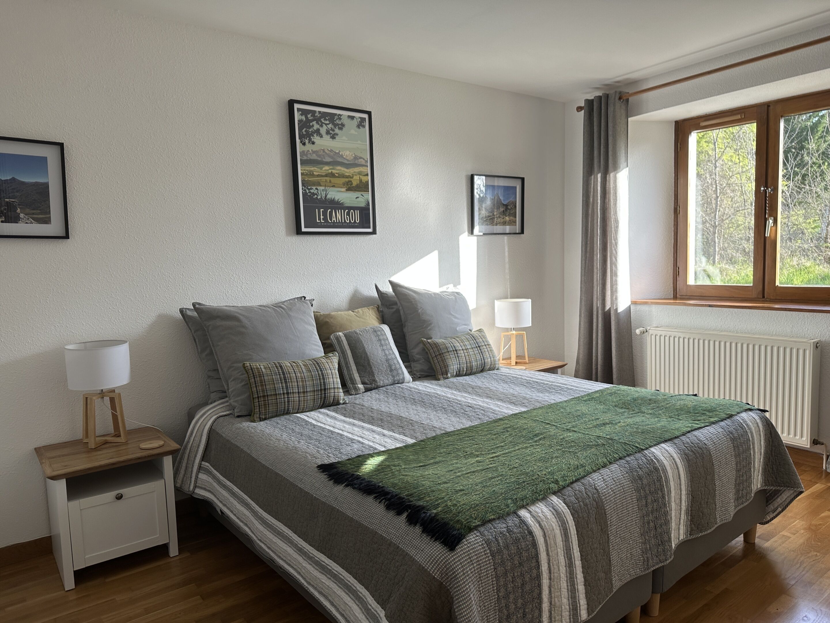 Ein Schlafzimmer mit einem Bett, zwei Nachttischen, einem Fenster mit Vorhängen und zwei gerahmten Bildern an der Wand.
