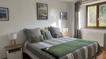 Ein Schlafzimmer mit einem Bett, zwei Nachttischen, einem Fenster mit Vorhängen und zwei gerahmten Bildern an der Wand.