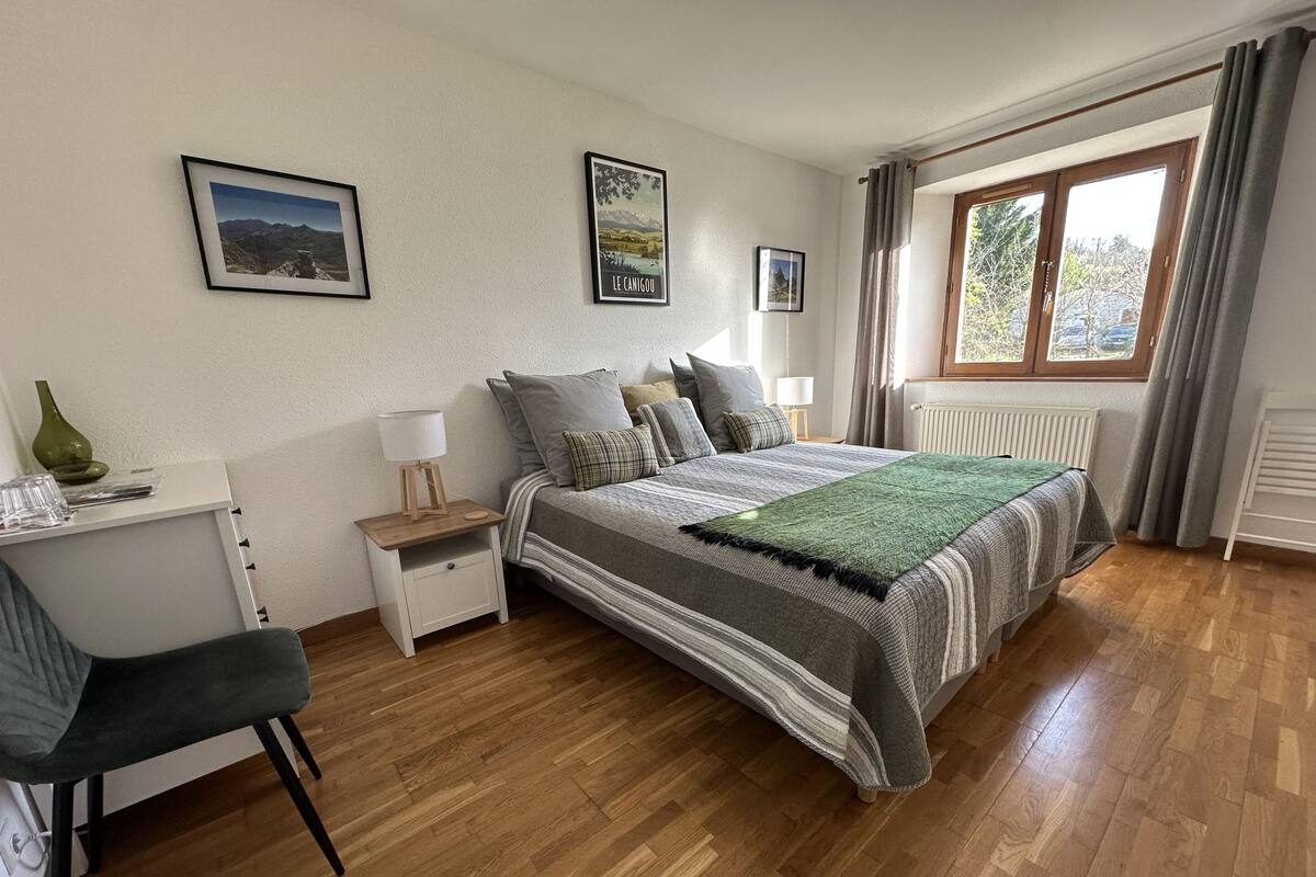 Un dormitorio con cama, mesitas de noche, un escritorio y una silla. Dos cuadros enmarcados adornan la pared.