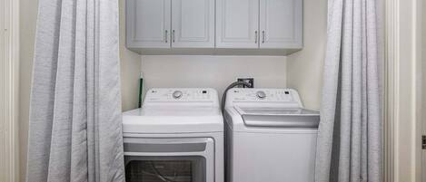 Un cuarto de lavandería con dos lavadoras blancas y un gabinete encima.