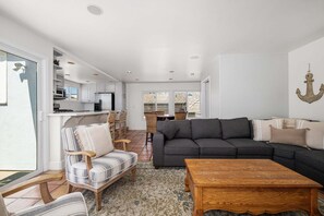 A living room with a sofa, chairs, a wooden coffee table, and a kitchen area with a dining table.