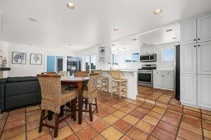 A modern kitchen with white cabinets, a dining area with wicker chairs, and a gray sofa.