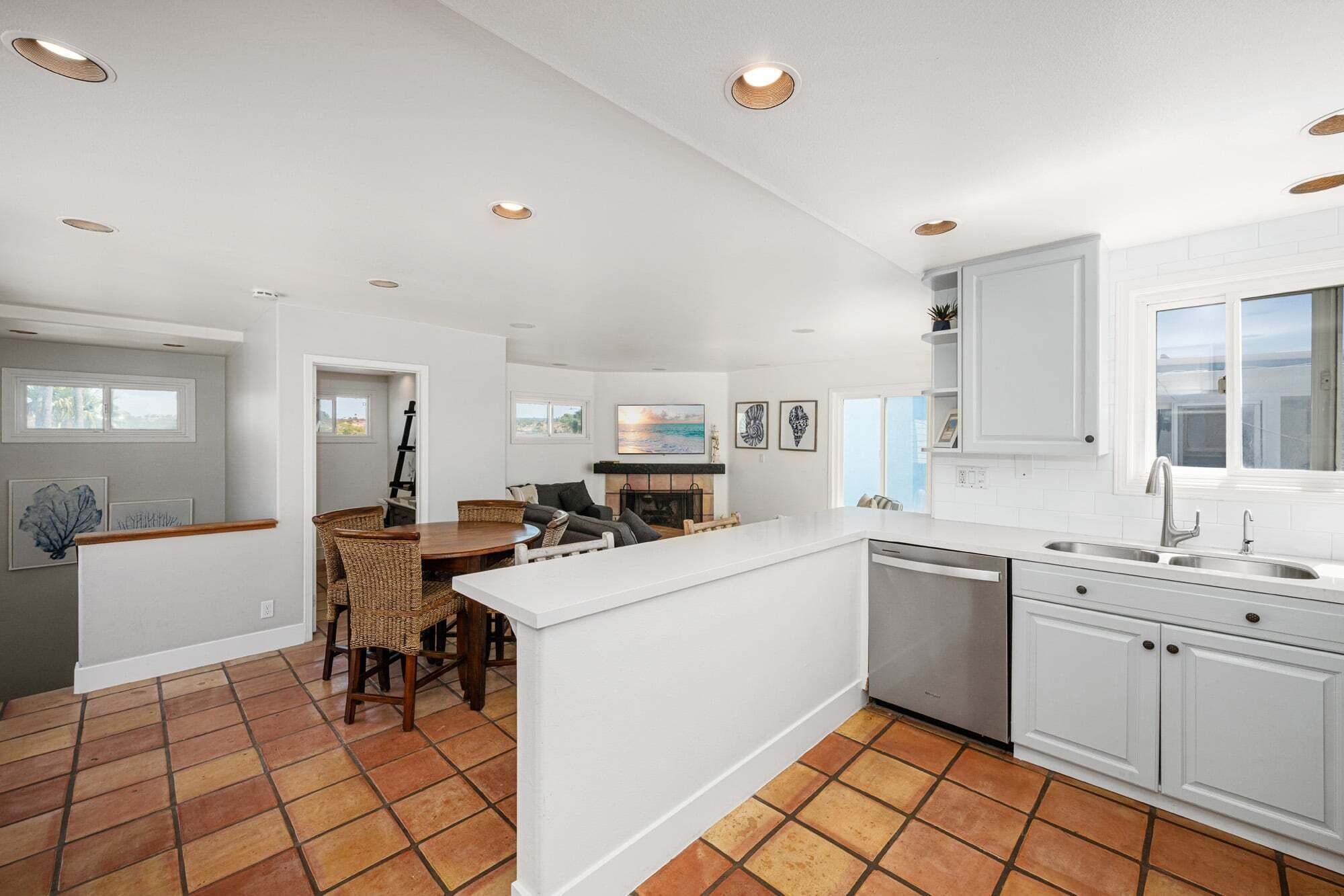 A modern kitchen with white cabinetry, a central island, and a dining area with wicker chairs.