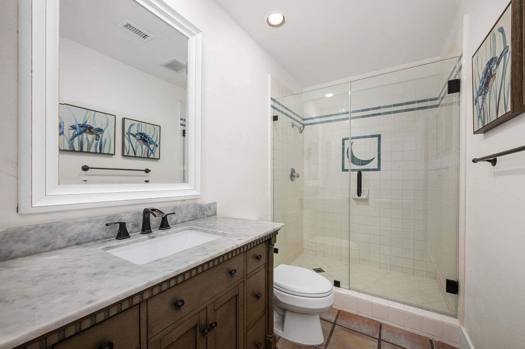A bathroom with a marble countertop, a white sink, a toilet, and a glass-enclosed shower.