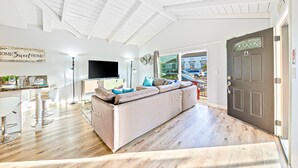 Ein modernes Wohnzimmer mit einer Couch, einem Essbereich mit Barhocker, einem Flachbildfernseher und einer Tür zum Außenbereich.
