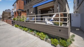 Un bâtiment moderne à deux étages, doté d’un espace extérieur couvert avec des sièges, d’une cheminée en briques et d’une rangée de plantes en pot le long du trottoir.
