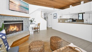 Un salon moderne doté d’une cheminée, d’un coin repas et d’une cuisine avec des armoires blanches et un plafond en bois.