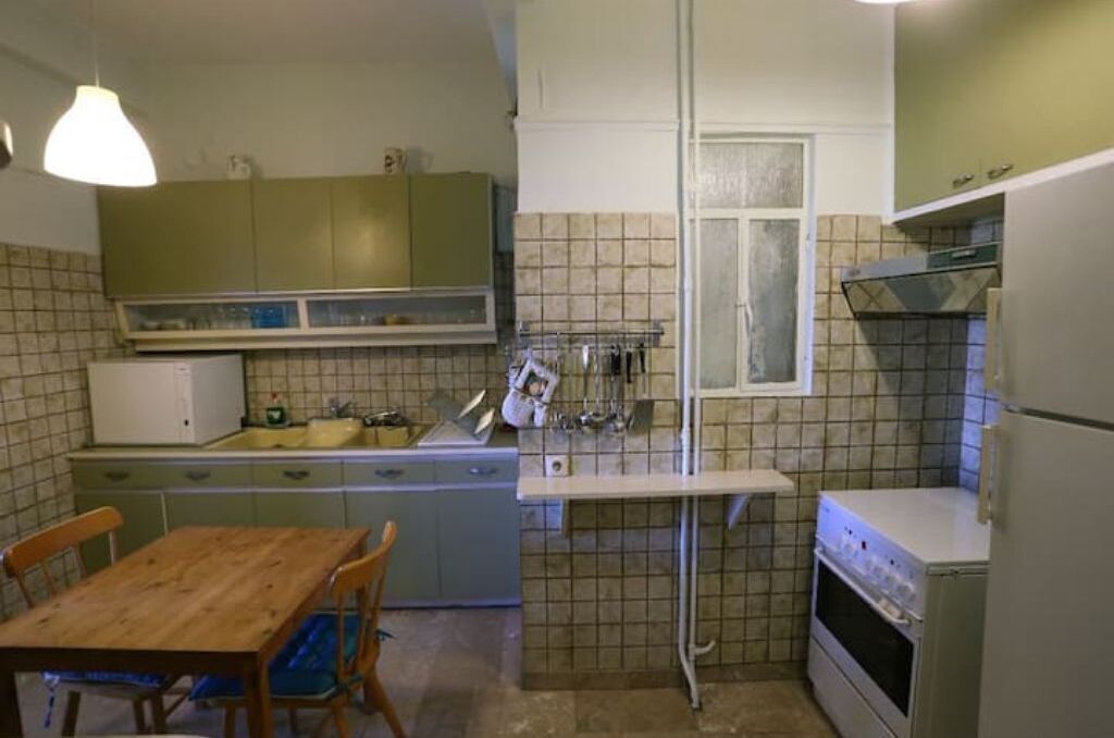 A compact kitchen with a wooden table and chairs, a built-in oven, and a window.