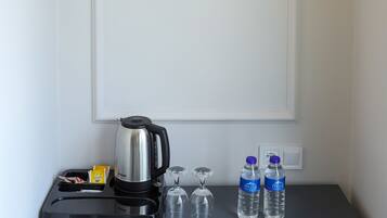 Habitación de hotel con una lámpara de pared, una cafetera, dos tazas, dos botellas de agua y un vaso.