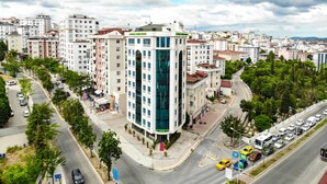 A modern hotel with a prominent glass facade, surrounded by a cityscape with various buildings and a busy street. - Fontana Verde (Istanbul)