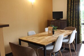 A conference room with a wooden table, white chairs, a potted plant, a television on a cabinet, and a window with curtains. - Floor -2, view valley, swimming pool, hammam, terrace, parking, tv, 50m², Pra Loup (Jausiers)