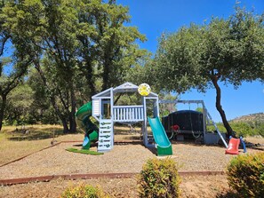 Un parque infantil con un tobogán, estructura para escalar y una zona cubierta.