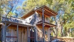 Eine rustikale Holzhütte mit Veranda und überdachter Terrasse, umgeben von Bäumen.