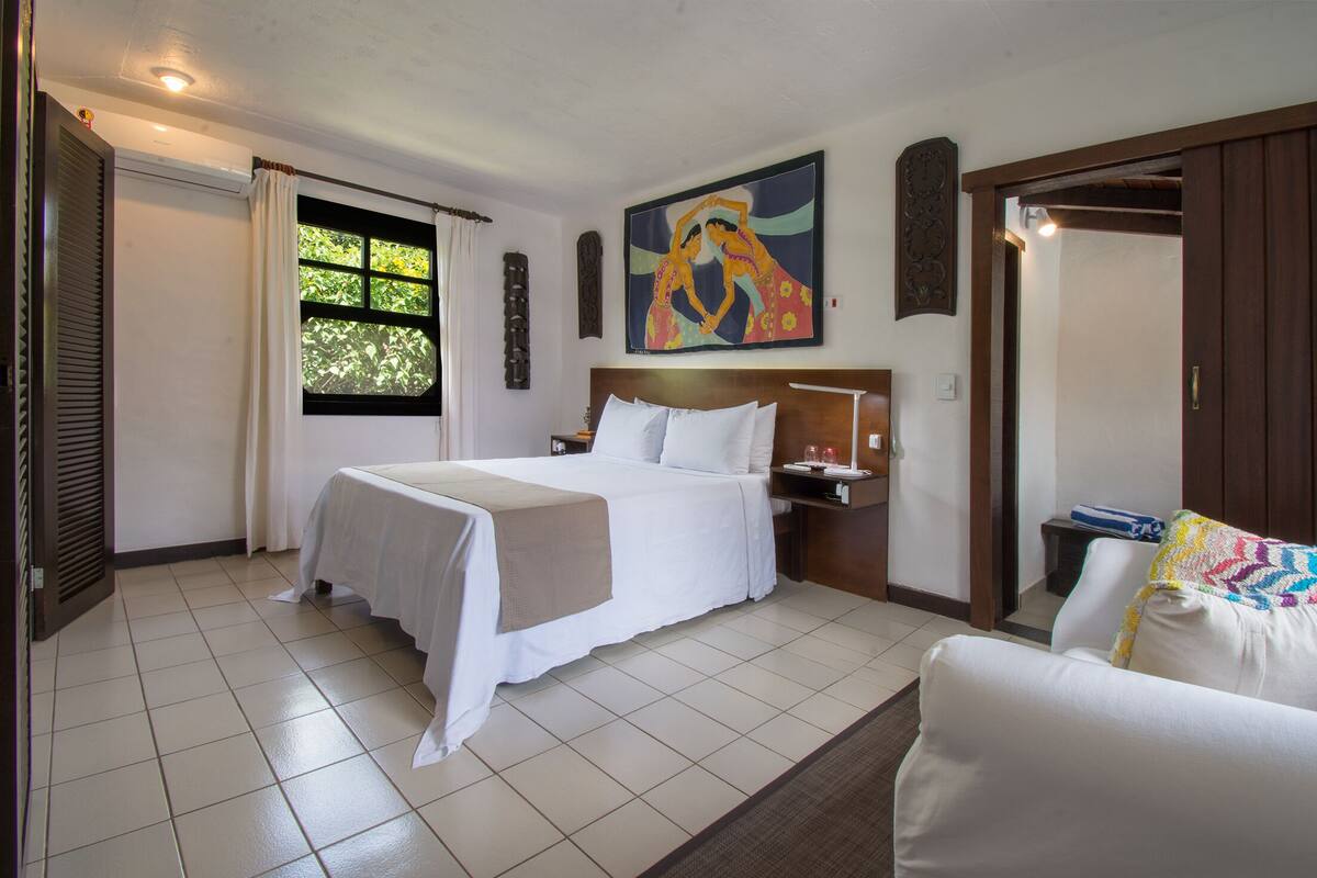 Une chambre d’hôtel avec un lit, une table de chevet, une fenêtre avec des rideaux, un tableau au mur et une porte.