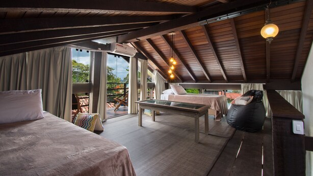 A spacious room with a large bed, a glass table, and a bean bag chair. There is a balcony with a view of the outdoors. - Pousada do Adriano (Búzios)