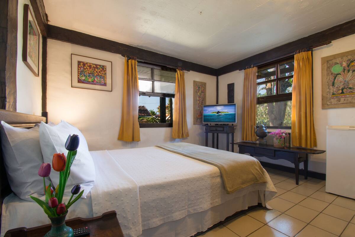 Une chambre d’hôtel avec un lit, une télévision, un vase de fleurs et des œuvres d’art accrochées aux murs.