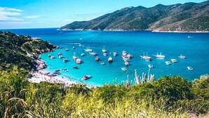 A coastal area with numerous boats anchored near the shore, surrounded by lush greenery and hills. - Pousada do Adriano (Búzios)