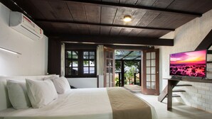 A bedroom with a bed, white bedding, a TV on a stand, and a view of the outdoors through a door. - Pousada do Adriano (Búzios)