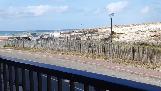 En kustväg med ett trästaket, en lyktstolpe och utsikt över stranden och havet.