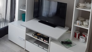 Ett modernt vardagsrum med en platt-TV, vita hyllor med dekorativa föremål och en tavla med en stadsbild ovanför TV:n.