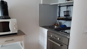 Ett kompakt kök med mikrovågsugn, spishäll, ugn och ett litet handfat.