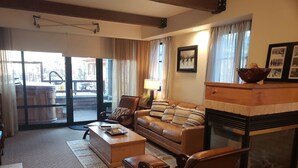 A cozy living room with a leather sofa, a coffee table, a fireplace, and a large window with curtains.
