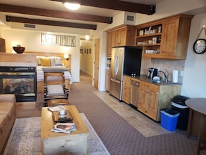 Cozy living space with a central seating area, fireplace, and kitchen featuring a refrigerator and stove.
