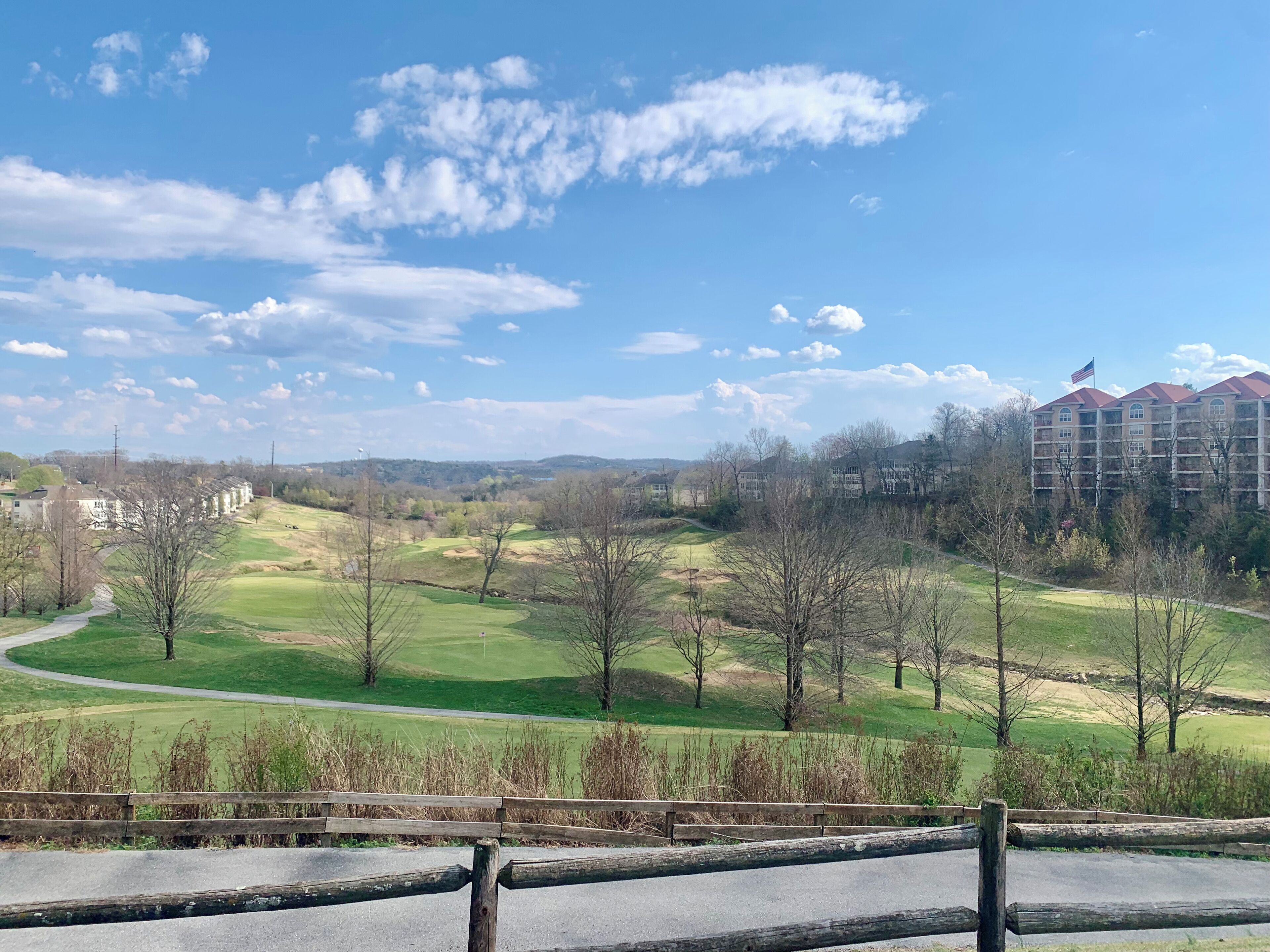 A golf course with a view of a multi-story building with a red roof and American flag.