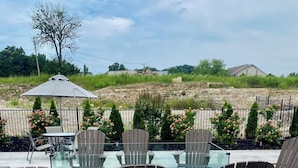 An outdoor patio with a glass-top table, four Adirondack chairs, and a decorative umbrella. - Three-unit SUPER PACKAGE! Sleeps 12. Three linked living, kitchen, and bedrooms. (Branson)
