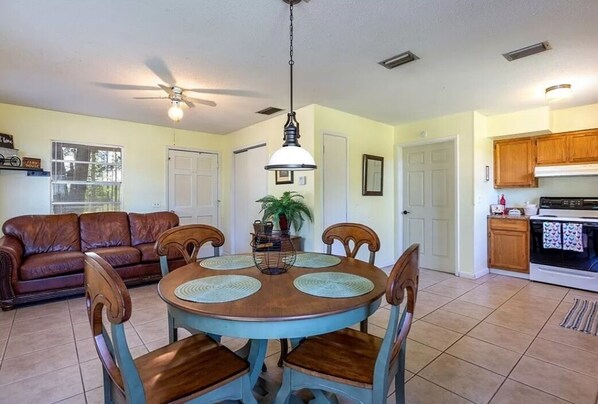 A dining area with a round table and chairs, a ceiling fan, and a kitchen in the background.
