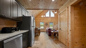 A wooden cabin interior with a kitchen, dining area, and a cozy living space.