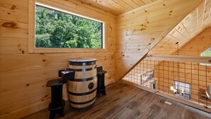 A wooden cabin with a large window, a wooden barrel, and a staircase.