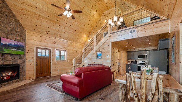 A spacious wooden cabin with a fireplace, a red sofa, a dining table with chairs, and a kitchen area.