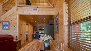 A wooden interior with a dining table set for two, a kitchen area, and a red couch.