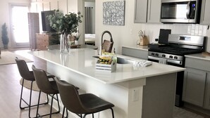 Une cuisine moderne dotée d’un grand îlot central, de tabourets de bar, d’un four à micro-ondes, d’une cuisinière et d’un évier.
