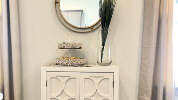 A white cabinet with a decorative mirror and a vase with green plants.