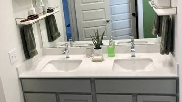 Une salle de bain avec deux lavabos, un grand miroir et une porte donnant sur une autre pièce.