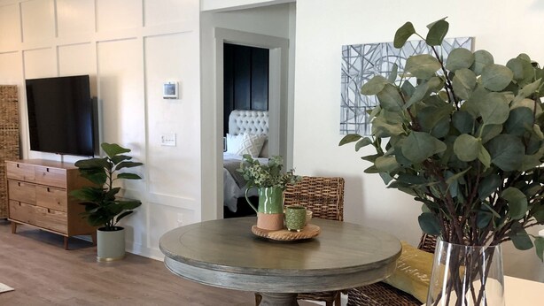 Un salon moderne avec une table ronde, un téléviseur fixé au mur, un canapé et une plante décorative.