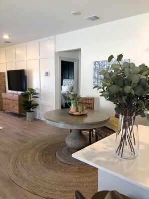 Un salon moderne avec une table ronde, un téléviseur fixé au mur, un canapé et une plante décorative.