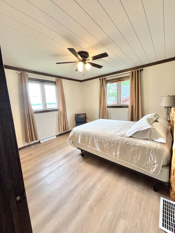 A bedroom with a bed, ceiling fan, windows with curtains, and a lamp. - Quiet retreat on Little Whitefish Lake (Garrison)