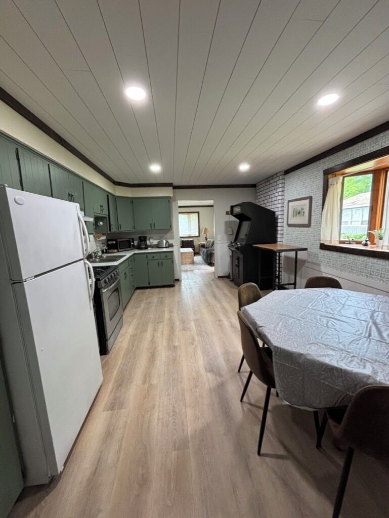 A kitchen with a refrigerator, stove, and sink, a dining table with chairs, and a grill outside.