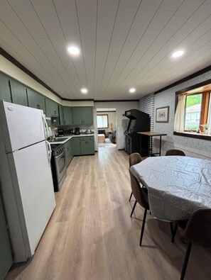 Une cuisine équipée d’un réfrigérateur, d’une cuisinière et d’un évier, une table à manger avec des chaises, et un barbecue à l’extérieur.