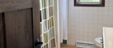 A bathroom with a wooden door, a shower curtain, a window, and a toilet.